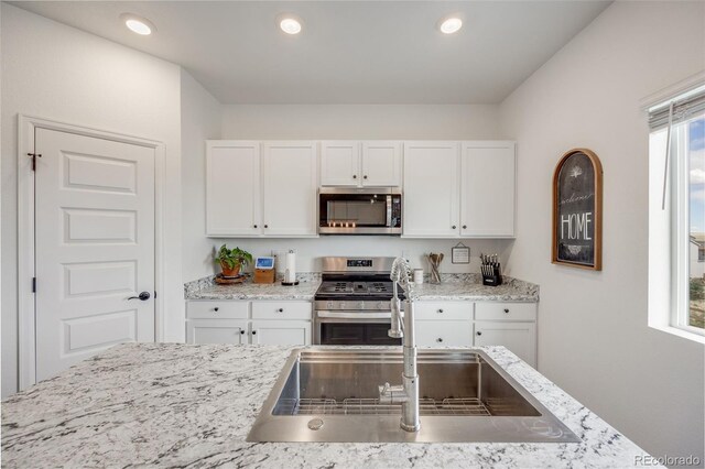 kitchen with stainless steel appliances, a sink, white cabinetry, light stone counters, and recessed lighting