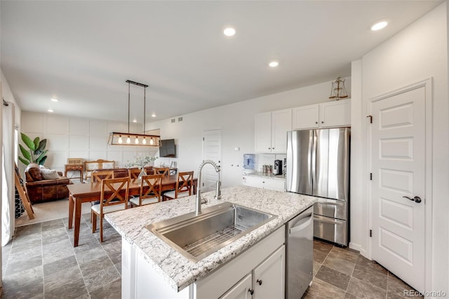 kitchen with stainless steel appliances, a sink, white cabinets, light stone countertops, and pendant lighting