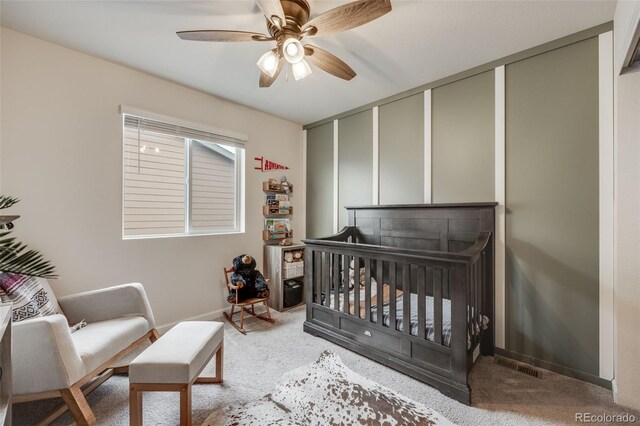carpeted bedroom featuring a nursery area, baseboards, and a ceiling fan