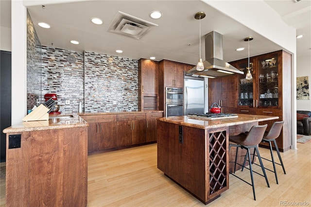 kitchen with hanging light fixtures, appliances with stainless steel finishes, a kitchen island, and island exhaust hood