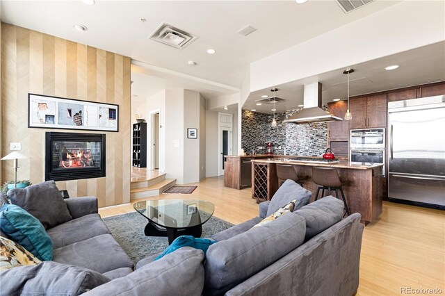 living area featuring light wood-style flooring, visible vents, a tiled fireplace, and recessed lighting