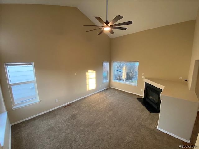 unfurnished living room featuring visible vents, ceiling fan, a fireplace with flush hearth, dark carpet, and high vaulted ceiling