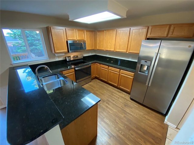 kitchen featuring light brown cabinetry, dark stone counters, light wood-type flooring, stainless steel appliances, and a sink