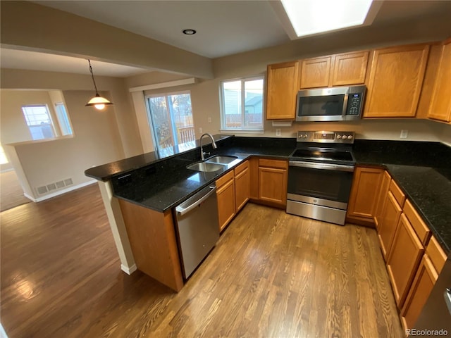 kitchen featuring visible vents, a sink, wood finished floors, stainless steel appliances, and a peninsula