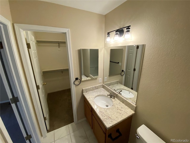 bathroom with a spacious closet, toilet, vanity, and baseboards