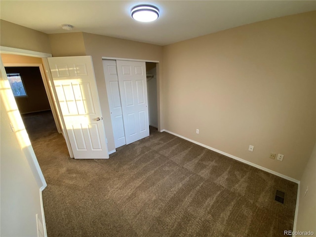 unfurnished bedroom with visible vents, dark colored carpet, a closet, and baseboards