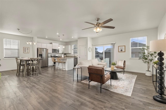 living room with ceiling fan with notable chandelier and dark wood-type flooring