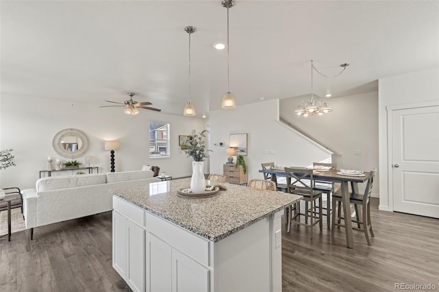 kitchen with dark hardwood / wood-style flooring, light stone counters, ceiling fan with notable chandelier, white cabinetry, and hanging light fixtures