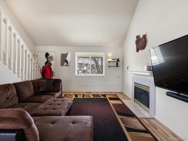 living room with light wood finished floors, a tiled fireplace, stairway, vaulted ceiling, and a textured ceiling