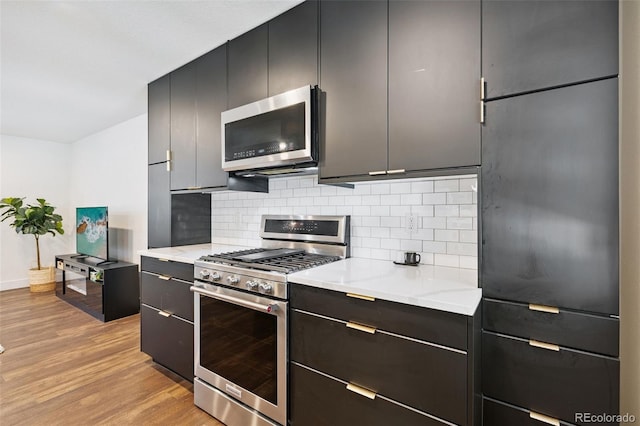 9563 W Caley Ave, Littleton, CO 80123 - kitchen with stainless steel appliances, light wood-style floors, decorative backsplash, modern cabinets, and dark cabinetry