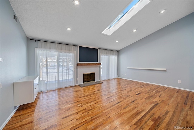 unfurnished living room featuring a textured ceiling, light hardwood / wood-style floors, and vaulted ceiling with skylight