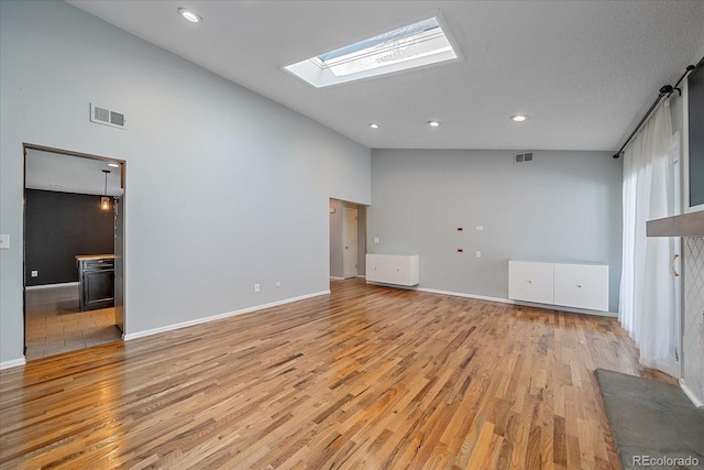 unfurnished living room with a skylight, light hardwood / wood-style flooring, and high vaulted ceiling