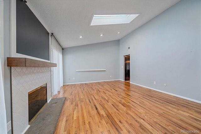 unfurnished living room with a skylight, light hardwood / wood-style floors, and a tiled fireplace