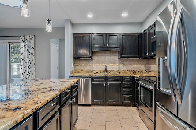 kitchen featuring decorative backsplash, appliances with stainless steel finishes, light stone counters, sink, and pendant lighting