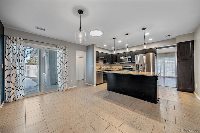 kitchen featuring light stone countertops, a center island, hanging light fixtures, backsplash, and appliances with stainless steel finishes