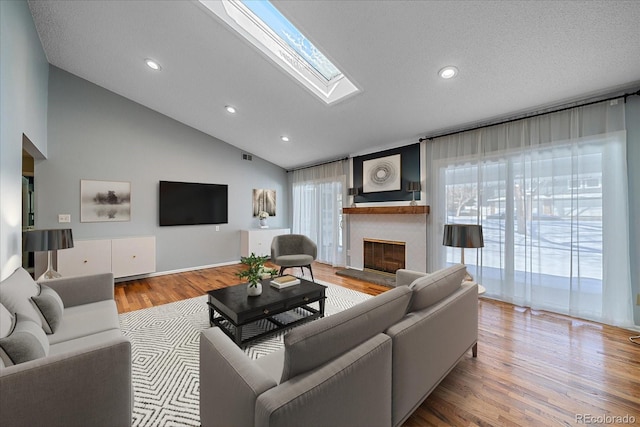living room featuring vaulted ceiling with skylight, recessed lighting, wood finished floors, and a fireplace