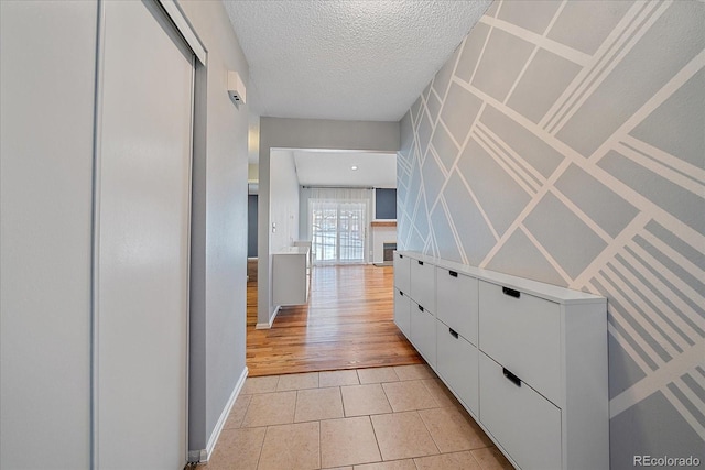 corridor with light tile patterned floors, baseboards, and a textured ceiling