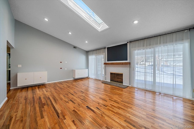 unfurnished living room featuring recessed lighting, a fireplace with raised hearth, light wood-style floors, visible vents, and lofted ceiling with skylight