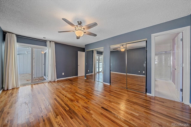 unfurnished bedroom featuring baseboards, two closets, a ceiling fan, a textured ceiling, and wood finished floors