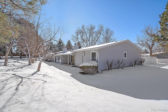 view of snowy exterior with fence and a chimney