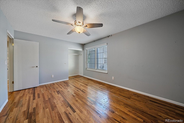 unfurnished bedroom featuring a textured ceiling, wood finished floors, baseboards, and a closet