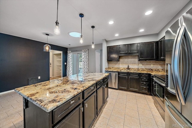 kitchen with a kitchen island, light stone counters, a sink, stainless steel appliances, and decorative backsplash