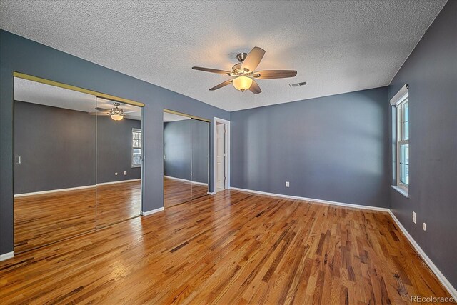 unfurnished room with visible vents, a textured ceiling, wood finished floors, and ceiling fan