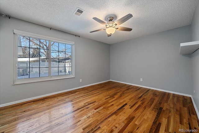 unfurnished room with a textured ceiling, wood finished floors, a ceiling fan, and visible vents