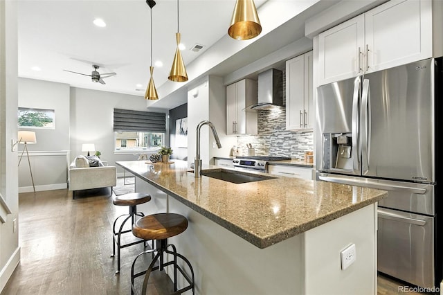 3431 W 16th Ave, Denver, CO 80204 - kitchen featuring appliances with stainless steel finishes, wall chimney exhaust hood, tasteful backsplash, a center island with sink, and light stone countertops