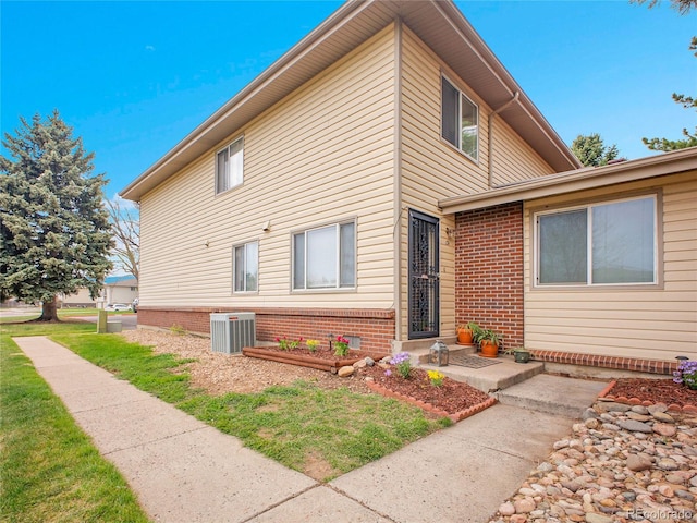 view of front of home with central AC, brick siding, and a front lawn