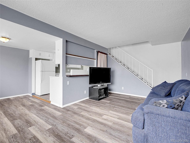 living room with baseboards, stairs, light wood finished floors, and a textured ceiling