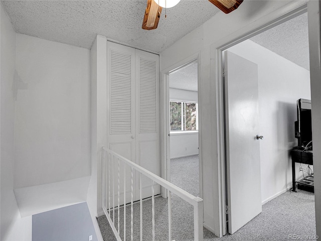 corridor featuring carpet flooring, a textured ceiling, an upstairs landing, and baseboards