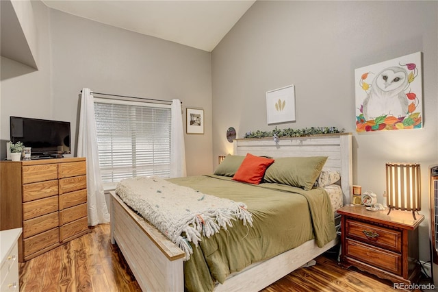 bedroom with high vaulted ceiling and wood finished floors