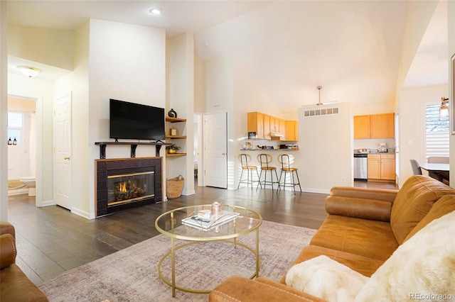 living room with high vaulted ceiling, a tile fireplace, and dark hardwood / wood-style floors