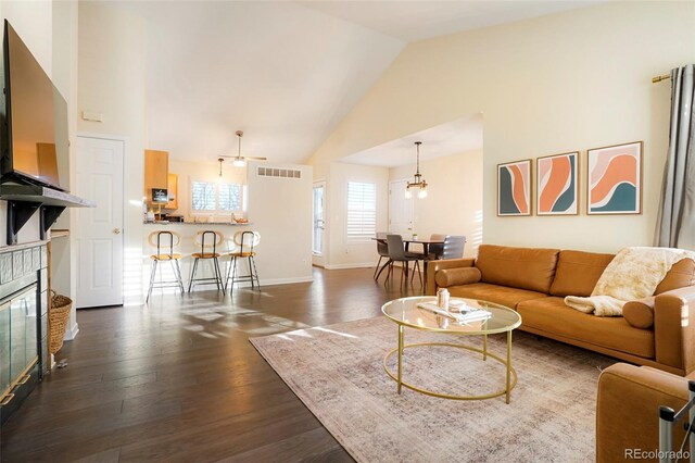 living room featuring dark wood-type flooring, ceiling fan with notable chandelier, and high vaulted ceiling