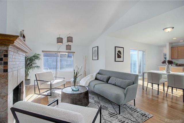 living area with a healthy amount of sunlight, a fireplace, light wood-style floors, and vaulted ceiling