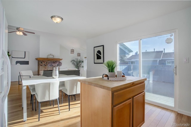 kitchen with a ceiling fan, light wood-type flooring, a kitchen island, brown cabinets, and butcher block counters