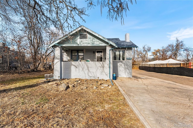 bungalow-style home featuring brick siding, a chimney, and fence