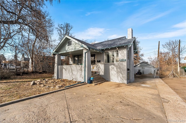 exterior space with driveway, a shingled roof, a chimney, and brick siding