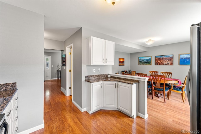 kitchen with white cabinetry, light wood-type flooring, kitchen peninsula, and stainless steel refrigerator