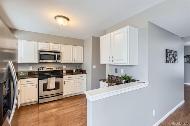 kitchen featuring appliances with stainless steel finishes, light wood-type flooring, baseboards, a peninsula, and white cabinetry