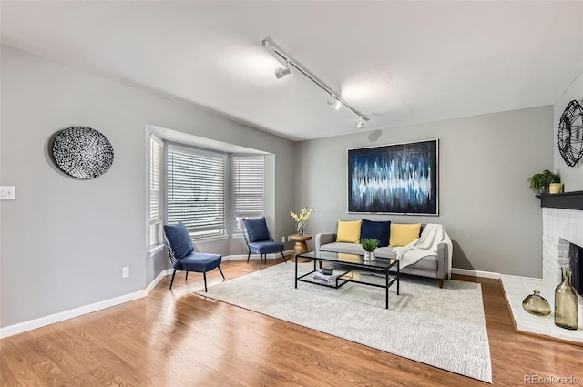 living room with baseboards, rail lighting, a brick fireplace, and wood finished floors