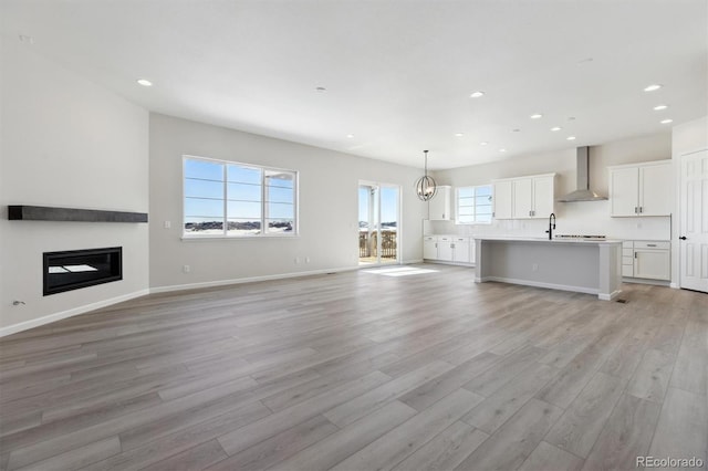 unfurnished living room with an inviting chandelier, sink, and light hardwood / wood-style floors