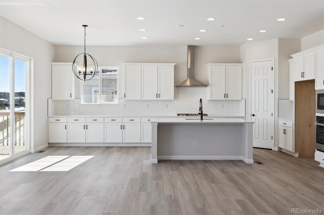 kitchen featuring white cabinetry, pendant lighting, wall chimney range hood, and light hardwood / wood-style floors