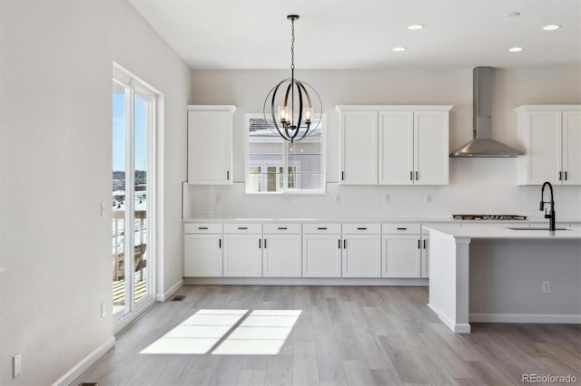 kitchen with a wealth of natural light, pendant lighting, white cabinetry, sink, and wall chimney exhaust hood