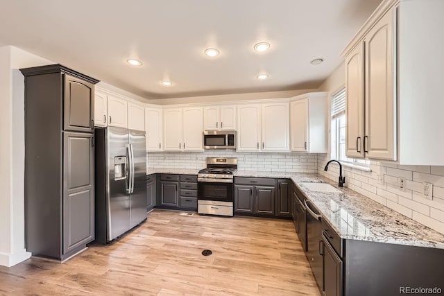 kitchen featuring gray cabinetry, sink, light stone counters, light hardwood / wood-style flooring, and appliances with stainless steel finishes