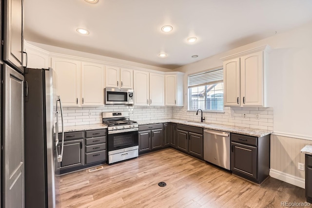 kitchen with sink, light stone countertops, light wood-type flooring, white cabinetry, and stainless steel appliances