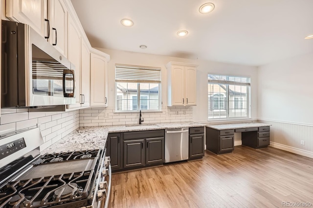 kitchen with light stone countertops, light wood-type flooring, stainless steel appliances, sink, and white cabinetry