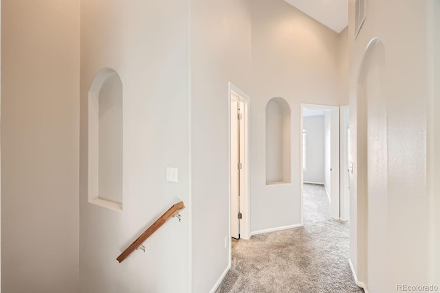 corridor featuring a towering ceiling and light colored carpet