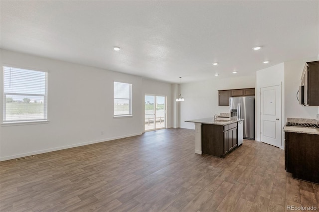 13487 Valentia St, Thornton, CO 80602 - kitchen with stainless steel appliances, light wood-type flooring, a center island with sink, dark brown cabinetry, and open floor plan